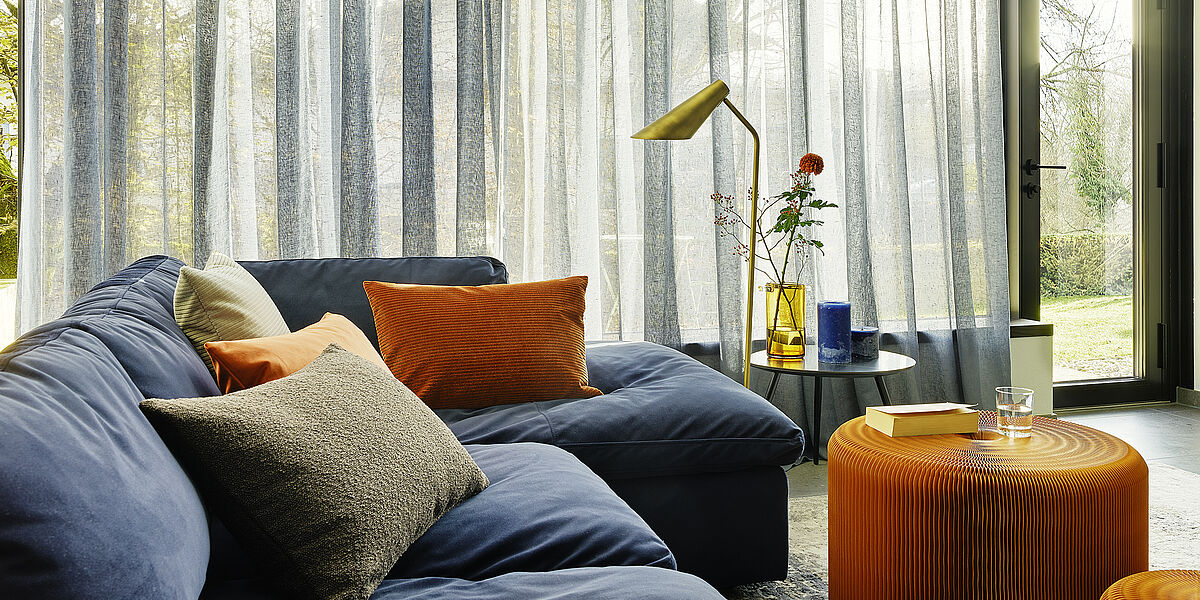 Wohnzimmer mit gemütlicher Couch und großem leicht transparenten Vorhang